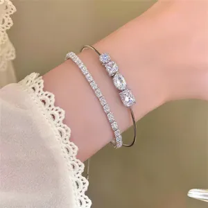 Nahaufnahme von silberfarbenen Armreifen mit klaren Zirkonia in verschiedenen Formen am Handgelenk.