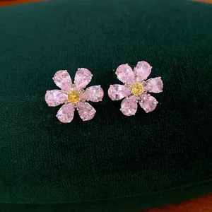 Close-up of elegant pink and yellow cubic zirconia flower stud earrings on green velvet