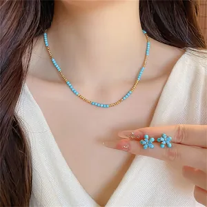 Gros plan de boucles d'oreilles fleurs turquoise et collier de perles sur un modèle.