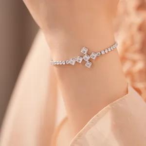 Detailopname van een zilverkleurige tennisarmband met een zirkonia kruismotief op de pols.