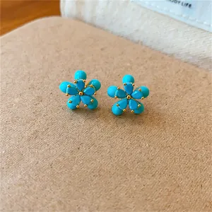 Gros plan d'élégantes boucles d'oreilles fleurs dorées avec pétales bleu turquoise.