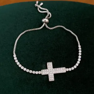 Gedetailleerde macro-opname van een zilveren kruisarmband met witte zirkonia steentjes.