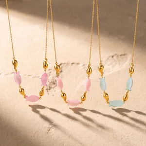 Close-up van goudkleurige viskettingen met roze en blauwe acrylbedeltjes op het strandzand.