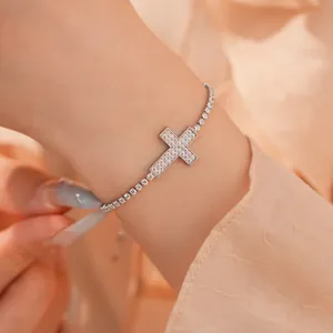 Close-up van een zilverkleurige tennisarmband met een kruisbedel bezet met zirkonia.