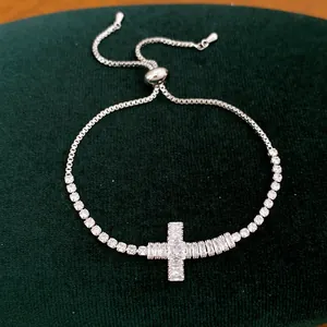 Detail van een zilveren verstelbare armband met een fonkelend kruis van zirkoon