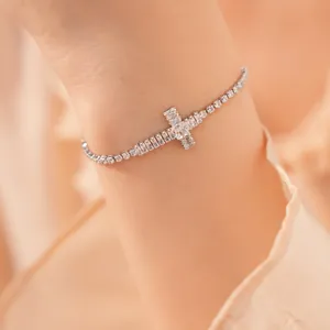 Detailopname van een zilveren kruisarmband met fonkelende zirkonia aan een vrouwelijke pols