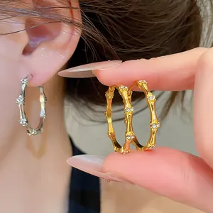 Close-up of elegant gold and silver bamboo-style hoop earrings with sparkling zircon accents