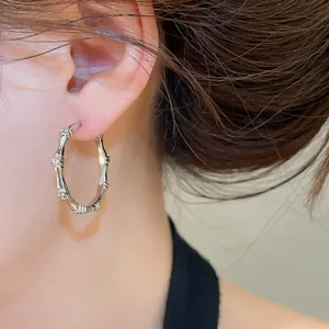 Close-up detail of silver bamboo hoop earrings with sparkling zircons worn on model ear.