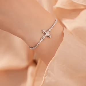 Close-up van een zilveren kruisarmband met zirkonia op een vrouwelijke pols.