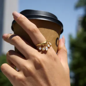 Detailansicht eines goldenen Wellenrings mit Zirkonia-Anhängern an einer Hand mit Kaffeetasse.