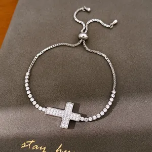 Close-up van zilveren kruisarmband met zirkonia steentjes op getextureerde achtergrond.