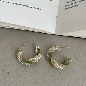 Détail macro de boucles d'oreilles torsadées plaquées or 14k avec émail vert et perles.