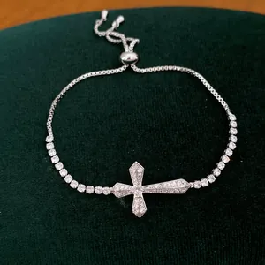Detailopname van een elegante zilveren kruisarmband met zirkonia op groen fluweel.