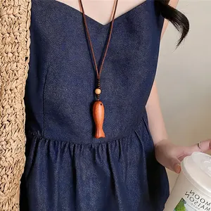 Nahaufnahme einer hölzernen Fisch-Halskette im Vintage-Stil zu einem dunkelblauen Kleid