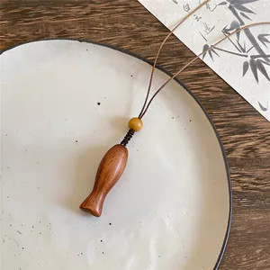 Detailansicht einer Holzhalskette mit Fischanhänger, feiner Holzmaserung und einer gelben Perle.