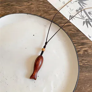 Detailaufnahme einer handgefertigten Holzhalskette mit Fischanhänger auf einem Keramikteller