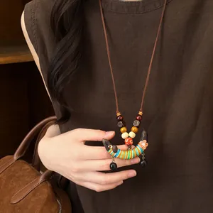 Détail rapproché d'un collier ethnique en perles de bois avec pendentif gousse coloré.