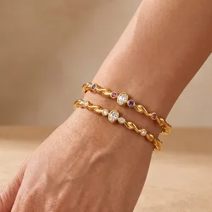 Gros plan détaillé de deux bracelets géométriques dorés avec des pierres colorées au poignet.