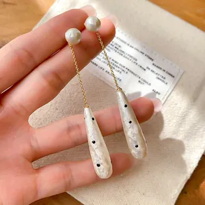 Close-up of vintage polka dot water drop pearl drop earrings held in hand.
