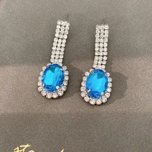 Detailansicht luxuriöser blauer ovaler Strass-Ohrhänger auf grauem strukturiertem Hintergrund