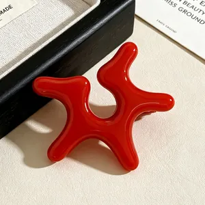 Detail view of vibrant red irregular starfish acrylic ear clip on beige background