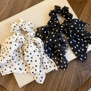 Detailed view of elegant black and white polka dot bow hair scrunchies on a white display board.