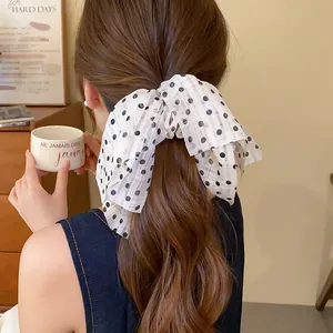 Close-up view of a white fabric polka dot bow hair scrunchie on a stylish brunette ponytail.