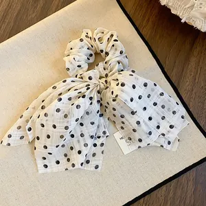 Close-up detail of off-white polka dot bow scrunchie with subtle plaid fabric texture