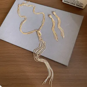 Detail van gouden meerstrengige geknoopte kwastjesketting en oorbellen op grijs bord