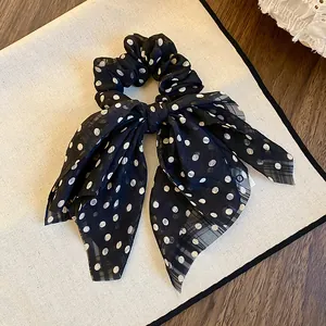 Detailed view of a black fabric bow scrunchie with classic white polka dot pattern
