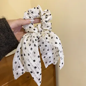Close-up of white fabric scrunchie with black polka dots and a decorative bow tie