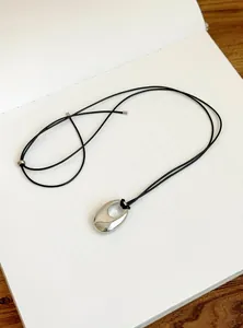 Detailansicht eines minimalistischen silbernen ovalen Anhängers an einer Kette.
