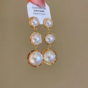 Vue détaillée de boucles d'oreilles triple perles dans des cadres dorés texturés