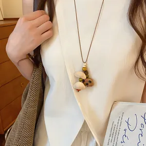 Detailopname van een handgemaakte houten berenketting gedragen op een witte blouse.
