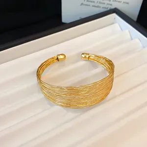 Close-up detail of a gold metallic multi-layer open cuff bracelet on a white tray
