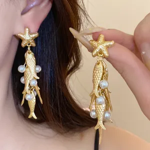 Close-up macro shot of elegant gold fish and starfish tassel earrings decorated with pearls