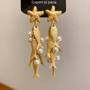 Detail shot of golden starfish and fish tassel earrings featuring white pearls and scales