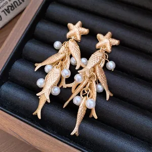 Detail view of gold starfish earrings with pearl-decorated fish tassels in a black box