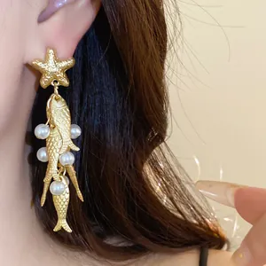 Close-up of gold starfish and pearl fish tassel earrings worn by a female model