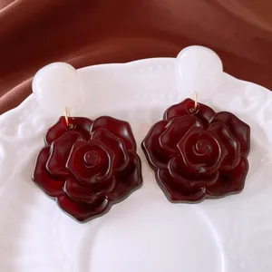 Makroansicht von Vintage-Harzrosen-Ohrringen mit dunkelroter Blume und weißem Bolzen