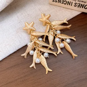 Macro view of elegant gold starfish earrings with dangling fish charms and white pearls.
