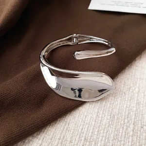 Close-up of a shiny silver geometric leaf bracelet on a textured brown fabric background