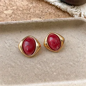 Primo piano di orecchini vintage dorati con resina marmorizzata rossa su un vassoio beige