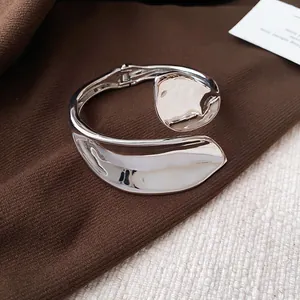 Detailed view of a polished silver geometric leaf-shaped open cuff bracelet on fabric