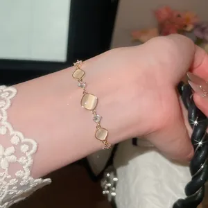 Detail van een goudkleurige armband met vierkante kattenoogstenen en fonkelende zirkoon.