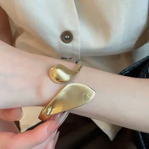 Macro view of a gold-tone matte geometric leaf open cuff bracelet on a woman's wrist