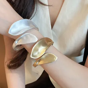 Detailed macro view of organic leaf-shaped metal cuff bracelets in gold and silver finishes