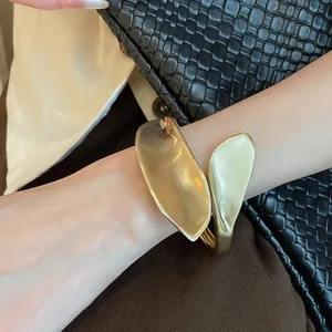 Detailed view of a matte gold leaf-shaped open cuff bracelet worn on the wrist.