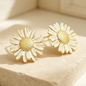 Détail rapproché de boucles d'oreilles marguerite en émail blanc et cœur doré