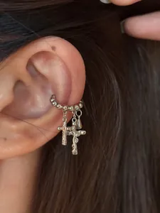 Detailaufnahme eines silberfarbenen Ohrklemmen mit Kreuz- und Tropfenanhängern am Ohr